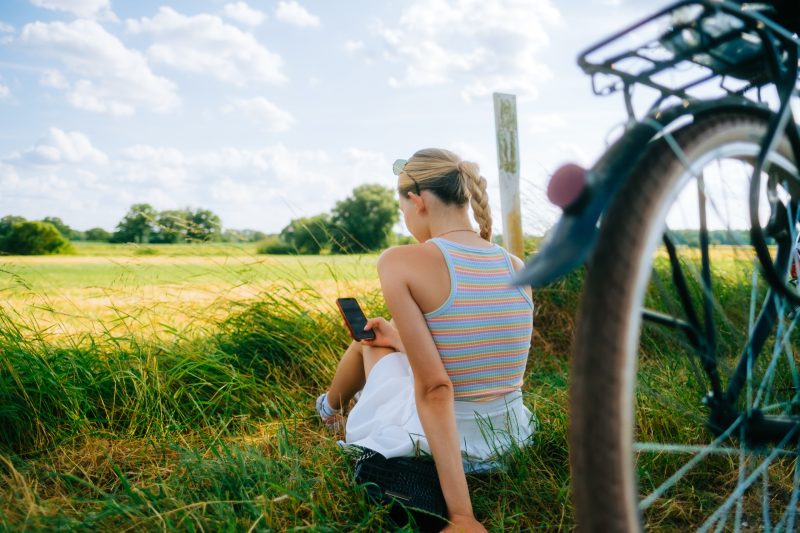young woman sitting in the grass next to her bicycle looking at her cell phone